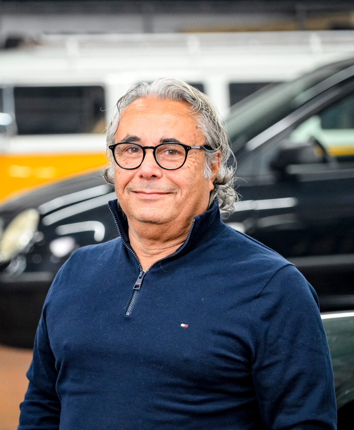 Person in dunkelblauem Pullover, im Hintergrund ein gelber VW-Bus und ein schwarzes Fahrzeug.