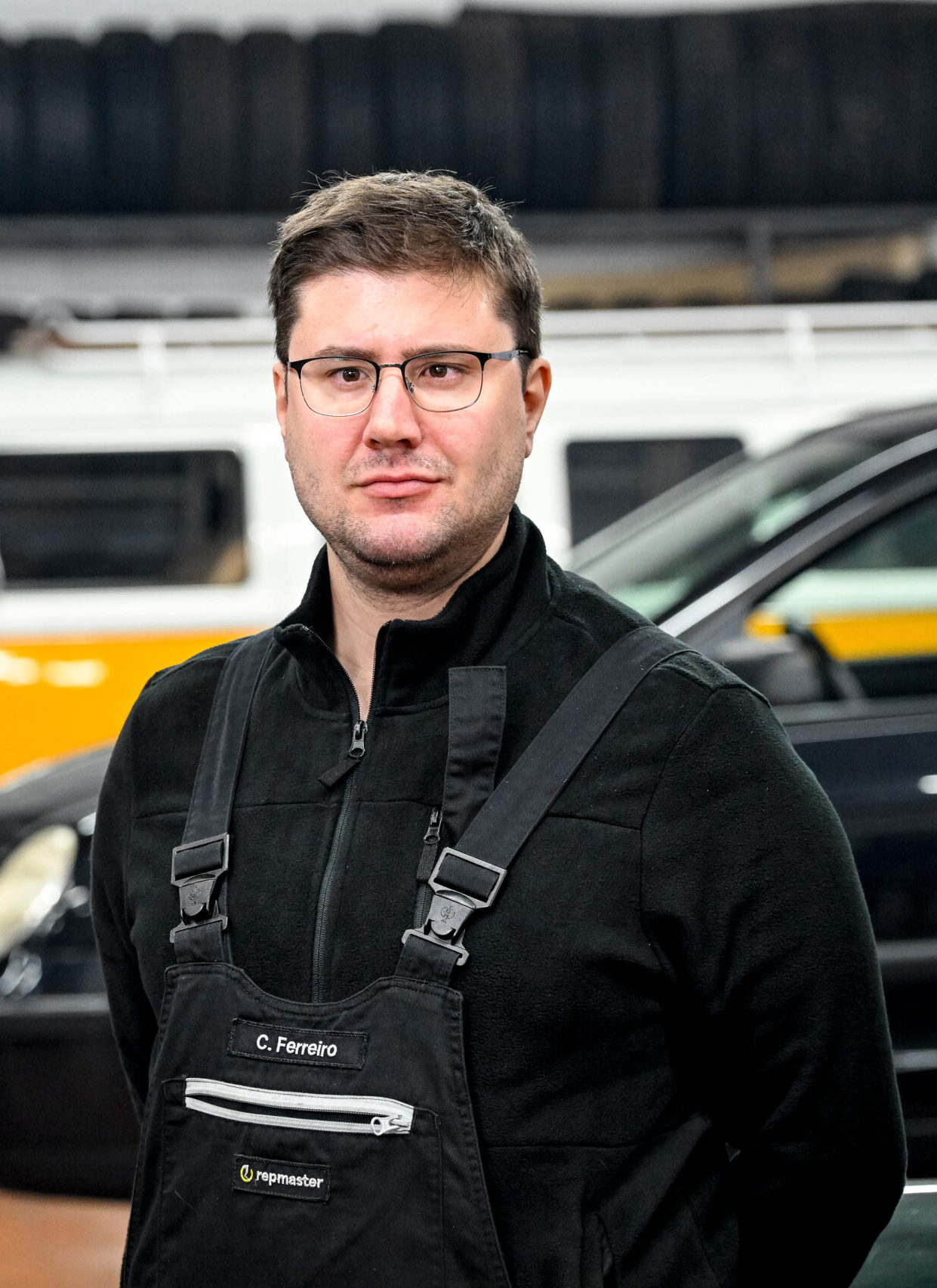 Person in schwarzer Arbeitskleidung mit Namensschild „C. Ferreiro“, im Hintergrund ein gelber VW-Bus und ein schwarzes Fahrzeug.