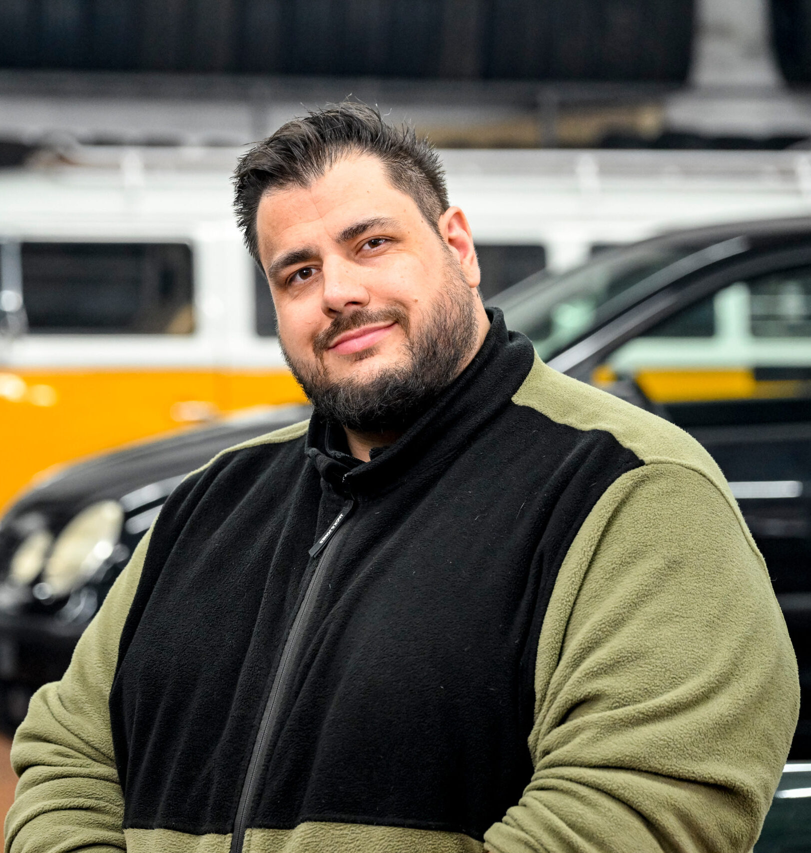 Person in einer Werkstatt, im Hintergrund ein gelber VW-Bus und ein weiteres Fahrzeug.